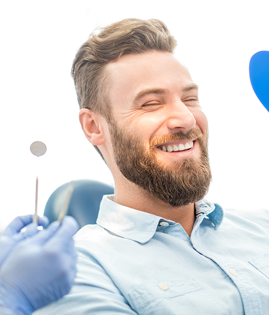 A smiling man in a dental chair, holding a toothbrush and wearing a blue face mask.